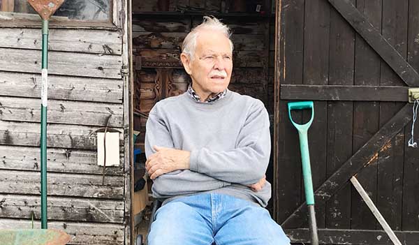 man sitting with garden tools outside shed