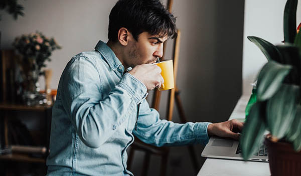 man drinking tea looking at computer