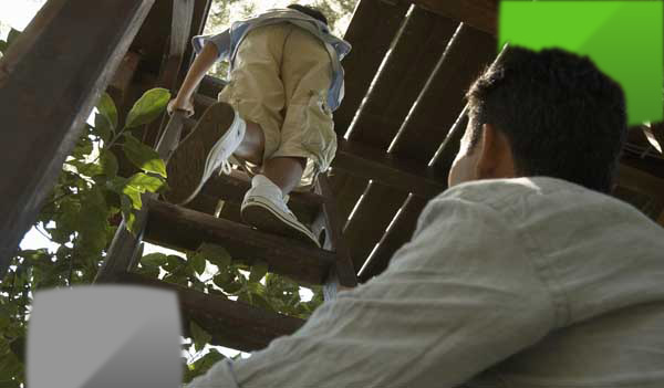 Boy climbing into treehouse whilst father watches