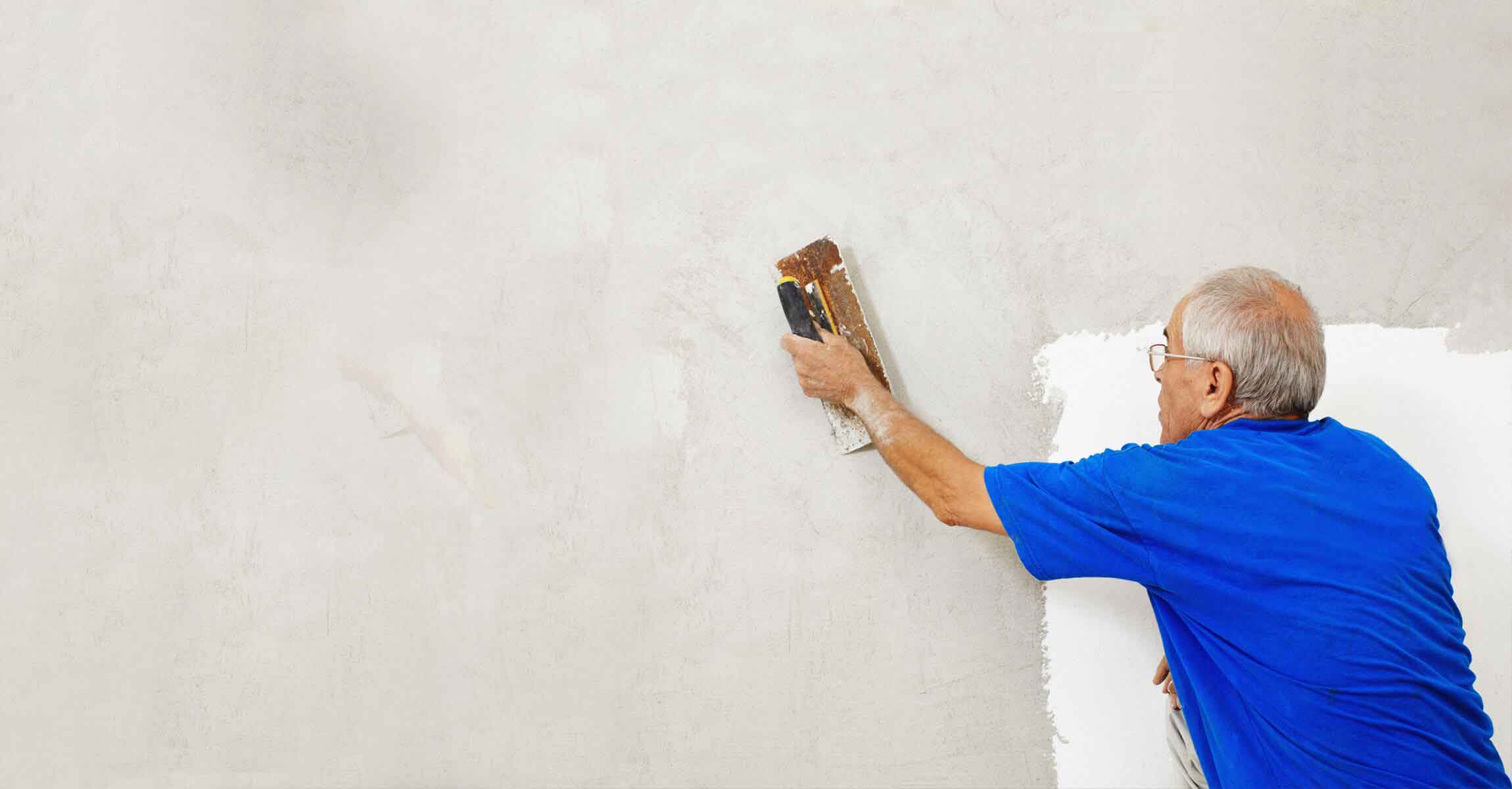 man in blue tshirt scraping wall for redecorating