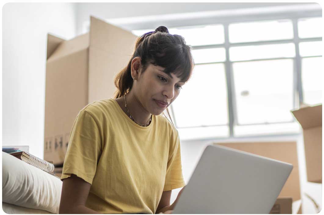Woman wearing yellow top on laptop next to boxes